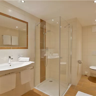 Ein modernes Badezimmer mit einer gläsernen Dusche und einem Waschbecken. Helle Fliesen und eine klare, minimalistische Einrichtung sorgen für ein sauberes Ambiente.