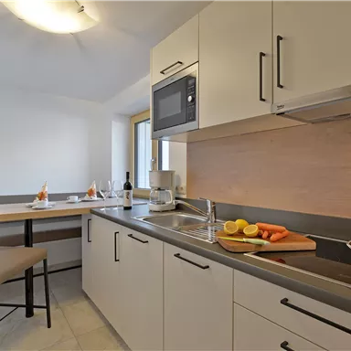 Eine moderne Küche mit einer hellen Farbgestaltung. Auf der Arbeitsplatte liegen frisches Gemüse und eine Kochplatte.