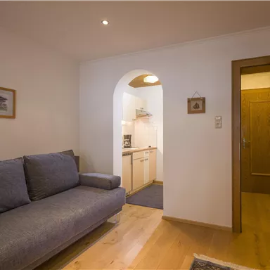 Ein gemütliches Wohnzimmer mit einem grauen Sofa und einem hölzernen Eingang zu einer Küche. Das Raumdesign ist modern und einladend.