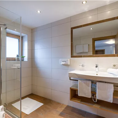 Ein modernes Badezimmer mit einer Dusche und einem großen Spiegel. Es gibt helle Fliesen und handtücher auf einem stilvollen Waschbecken.