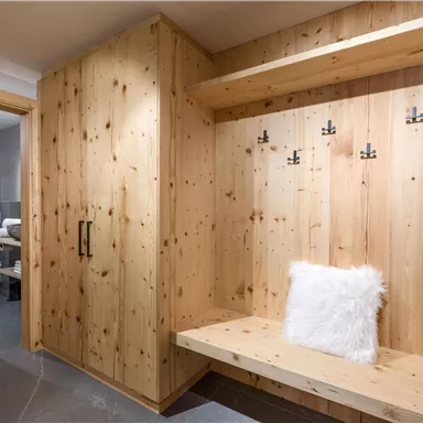 Ein gemütlicher Eingangsbereich mit Holzverkleidung und einer Sitzbank. An der Wand hängen mehrere Haken für Jacken und Mäntel.