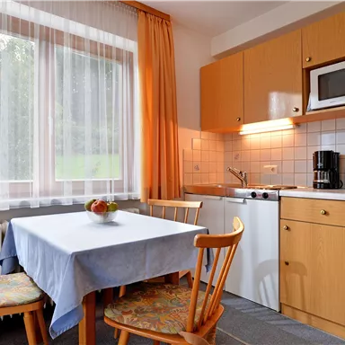 A cozy kitchen with a table and chairs. The amenities include a refrigerator, a microwave, and a kettle.