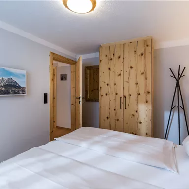 Ein gemütliches Schlafzimmer mit einem großen Bett und Holzregalen. Im Hintergrund gibt es ein Bild von Bergen und eine stilvolle Stehlampe.