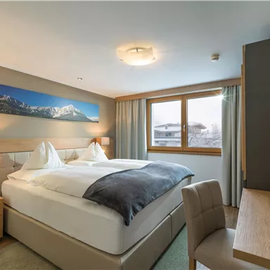 Ein modernes Zimmer mit einem großen Doppelbett und Holzdetails. Durch das Fenster hat man einen Blick auf die Berge.