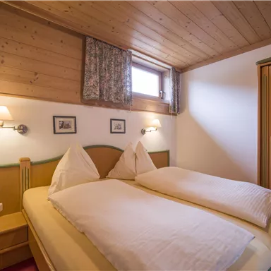 Ein gemütliches Schlafzimmer mit einem Doppelbett und Holzwänden. Es gibt Fenster mit Vorhängen und einen Kleiderschrank.