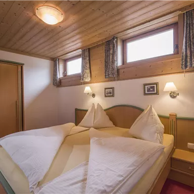 Ein gemütliches Schlafzimmer mit zwei Betten und Holzdecke. Es gibt Fenster mit Vorhängen und einen Kleiderschrank im Raum.