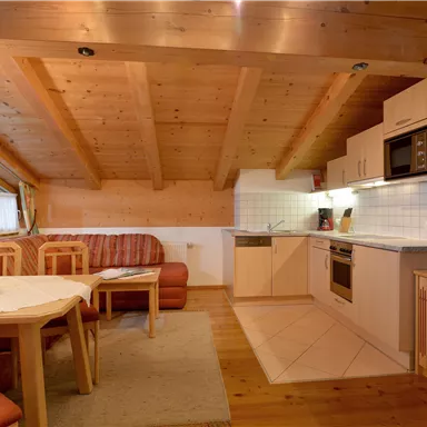 Eine gemütliche Küche mit Holzdecke und modernen Geräten. Der Wohnbereich ist hell und einladend, mit einem Tisch und einer Couch.