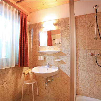 A bright bathroom with a shower, sink, and a mirror. The walls are painted in a warm, neutral tone, and the room has plenty of natural light.