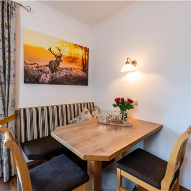 Ein gemütlicher Essbereich mit einem Holzstisch und Bänken. An der Wand hängt ein Bild eines Rehs vor einem Sonnenuntergang.