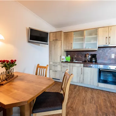 Eine moderne Küchenzeile aus Holz mit einem Tisch und Stühlen. Die Ausstattung umfasst einen Fernseher und eine Kaffeemaschine.