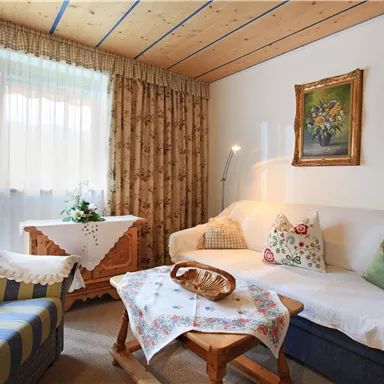 A cozy living room with a white sofa and blue accents. There is a small table with a floral arrangement and a beautiful mural.