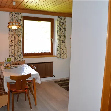 Eine gemütliche Küche mit einem Esstisch und Stühlen. Die Wände sind mit Blumenmustern dekoriert und ein Fenster lässt viel Licht herein.