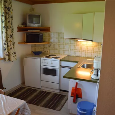 Eine moderne Küche mit weißen Schränken und einer grünen Arbeitsfläche. Die Küche ist hell und freundlich, ausgestattet mit grundlegenden Geräten.