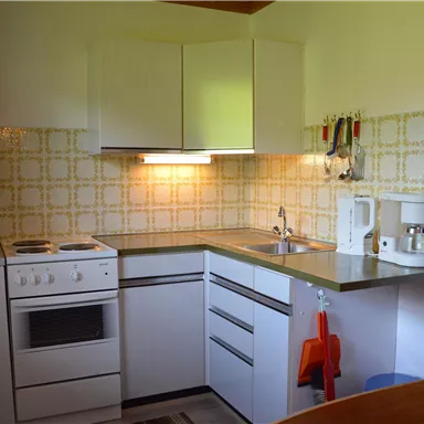 Eine kleine, moderne Küche mit weißen Möbeln und einem stilvollen Fliesendesign. Sie ist ausgestattet mit einem Herd, einer Spüle und verschiedenen Küchengeräten.