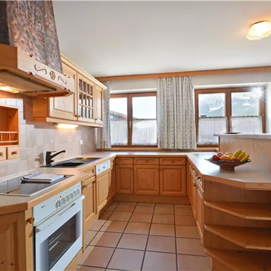 A modern kitchen with wooden cabinets and large windows. On the kitchen island, there is a bowl of fresh fruit.