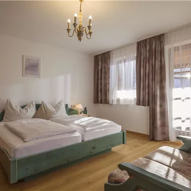 A cozy bedroom with two beds and a wooden cupboard. Large windows let in plenty of daylight.