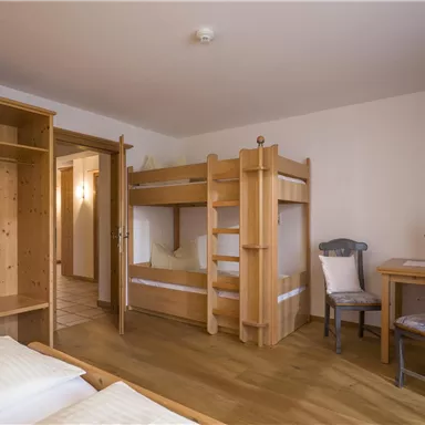 A cozy bedroom with a bunk bed and a table. The walls are light, and there is wooden furniture that creates a warm atmosphere.