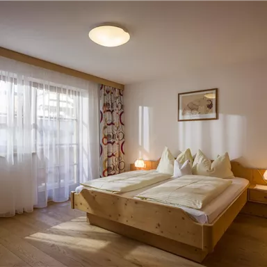 A cozy bedroom with a large bed and wooden details. Large windows allow for plenty of daylight.