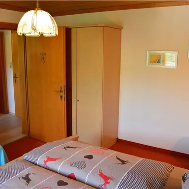 Ein gemütliches Schlafzimmer mit einem Doppelbett, einem Kleiderschrank und einer Holzdecke. Es gibt auch einen Sessel und einige Bilder an der Wand.