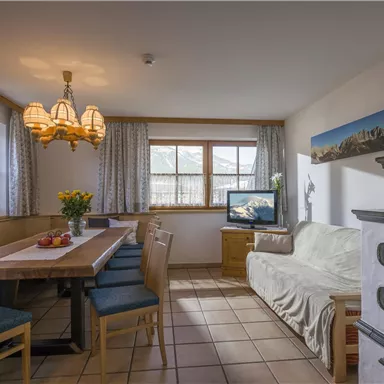 A cozy dining area with a large table and chairs. The room is brightly lit and has a window with an outward view.