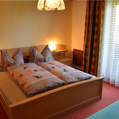 Ein gemütliches Schlafzimmer mit einem großen Bett und zwei Kissen. Der Raum hat ein Fenster mit Vorhängen und sanfter Beleuchtung.