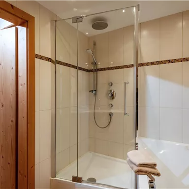 A modern bathroom with a glass shower enclosure and a bathtub. The walls are tiled and the door is made of wood.