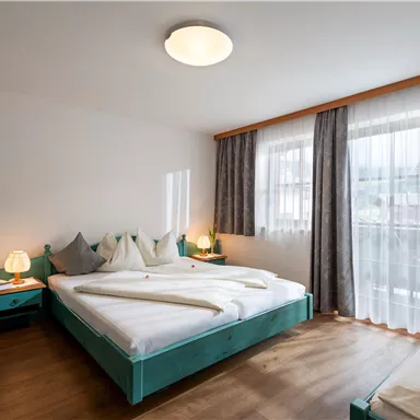 A modern bedroom with a large bed and an additional sleeping area. Bright curtains and wooden floors create a pleasant atmosphere.
