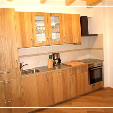 Eine moderne Küche mit Holzschränken und Edelstahlgeräten. Die Arbeitsfläche ist hell und übersichtlich gestaltet.