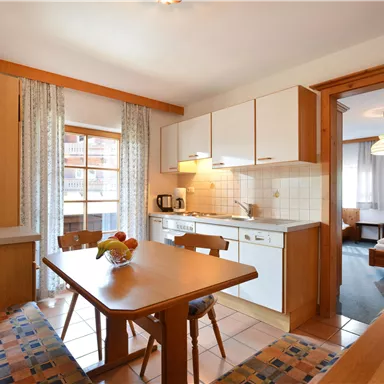 A cozy kitchen with a dining table and chairs. In the background, a bedroom is visible.