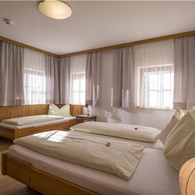 A bright room with two single beds and wooden details. The windows are covered with curtains and there is a cozy chair.