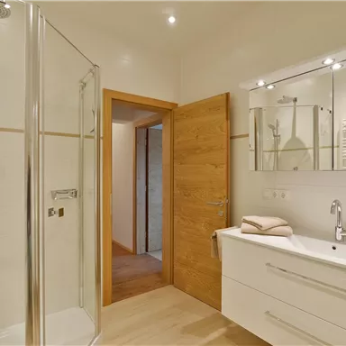 A modern bathroom with a glass shower and an elegant sink. The walls are light and the floor is made of wood.
