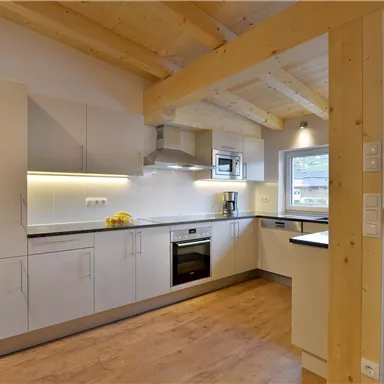 A modern kitchen with wooden ceilings and clear lines. The kitchen cabinets are in white, and the space is bright and welcoming.