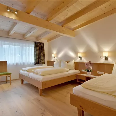 A cozy room with wooden paneling and two single beds. Large windows provide plenty of daylight.