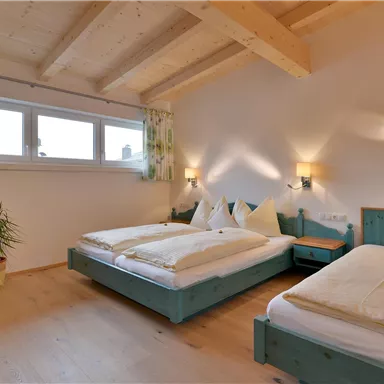 A cozy bedroom with two beds and wooden ceilings. Large windows provide plenty of daylight, and the decor is simple and inviting.