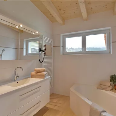 A modern bathroom with a bathtub and a sink. Large windows provide plenty of daylight and a fresh atmosphere.