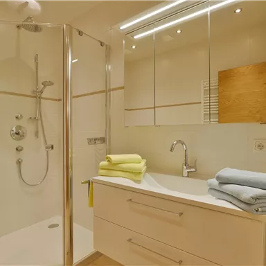 A modern bathroom with a glass shower and a sink. Colorful towels are neatly arranged on the rack.