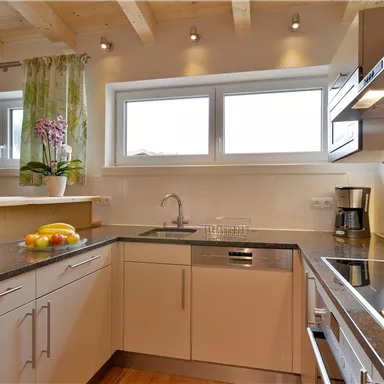 A modern kitchen with bright furniture and large windows. Fresh fruit and a coffee machine are on the countertop.