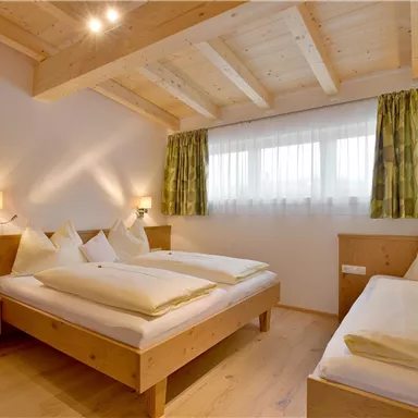 A cozy bedroom with two beds and wooden details. Bright curtains and soft light create an inviting atmosphere.