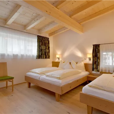 A cozy bedroom with two single beds and light wooden furniture. The large windows provide plenty of daylight.