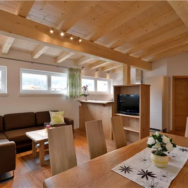 A modern living room with wooden ceilings and large windows. There is a sofa, a table, and a small bowl of flowers on the table.