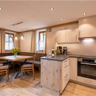 A modern kitchen with light furniture and wooden details. The dining table is cozily arranged and there are many windows for natural light.