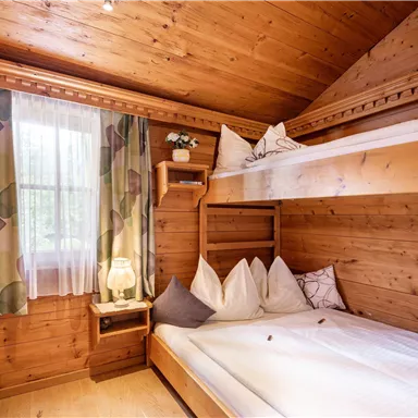 A cozy room with wood paneling and two beds. The windows let in a lot of light and the decoration is simple and inviting.