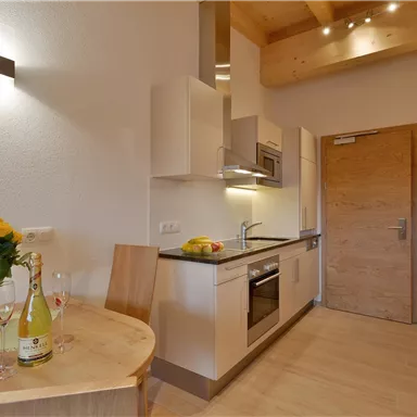 Modern kitchen with bright furniture and wooden ceilings. A table with flowers and drinks invites you to linger.