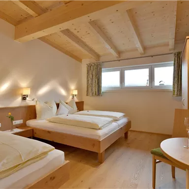 A stylish room with two beds and wooden ceilings. There is a small table with flowers and a cozy atmosphere.