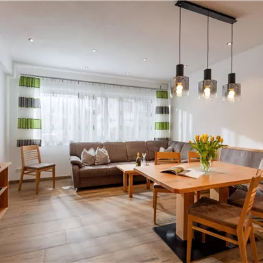 A cozy living space with a large table, chairs, and a comfortable couch. The windows let in plenty of daylight, and the decor is modern and stylish.