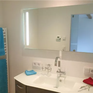 Ein modernes Badezimmer mit einem Waschbecken und einem Spiegel. Handtücher in Blau und Rot hängen an einem Handtuchhalter.