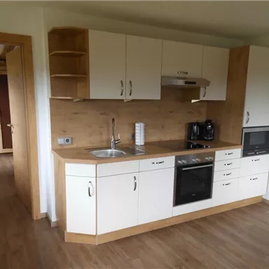 Eine moderne Küche mit Holzakzenten und weißen Schränken. Sie ist mit einem Herd, einem Kühlschrank und einer Spüle ausgestattet.