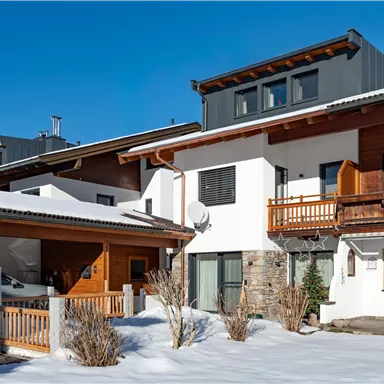 A modern house in the snow with a wooden balcony and clear blue sky. The surroundings feel calm and welcoming.