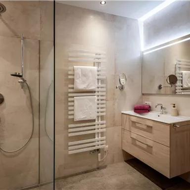 A modern bathroom with a large shower and an elegant wooden cabinet. The walls are in light tones, and there are fresh towels.