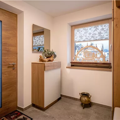 A modern entrance area with wooden details and a large window. The decor is designed to be simple and inviting.
